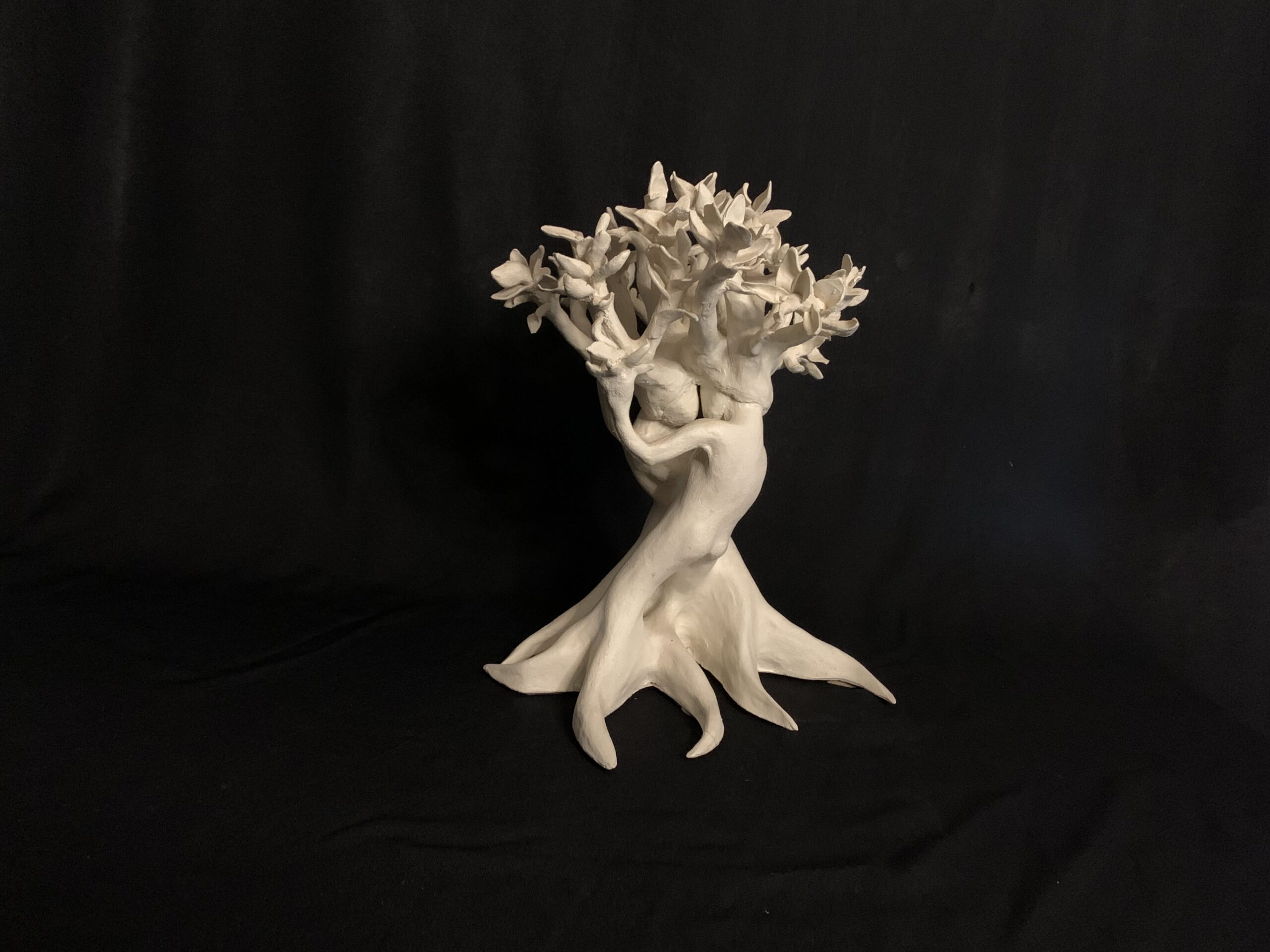 A white sculpture of two figures embracing, forming the trunk of a tree with branches at the top.