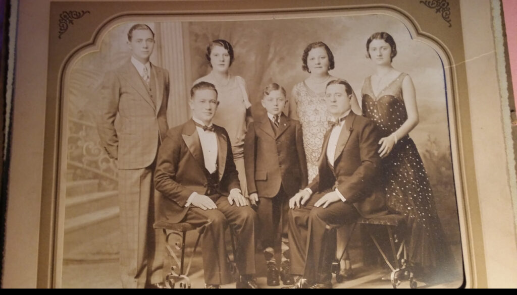 Vintage sepia photo of five adults and one child in formal attire, posing for a family portrait.