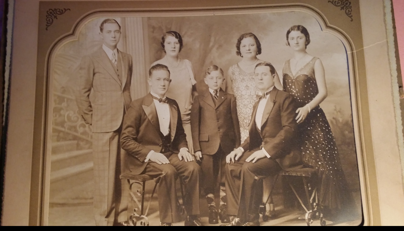 Vintage sepia photo of five adults and one child in formal attire, posing for a family portrait.