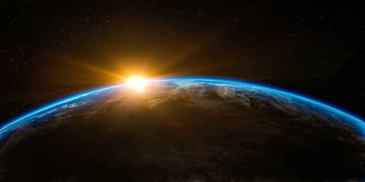 Sunrise over Earth seen from space with a bright glow at the horizon and stars in the background.