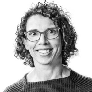 Smiling person with curly hair and glasses in a textured top, photographed in black and white.