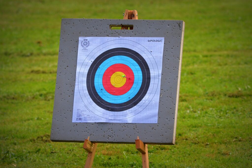 An archery target with colored rings stands outdoors on a grassy field.