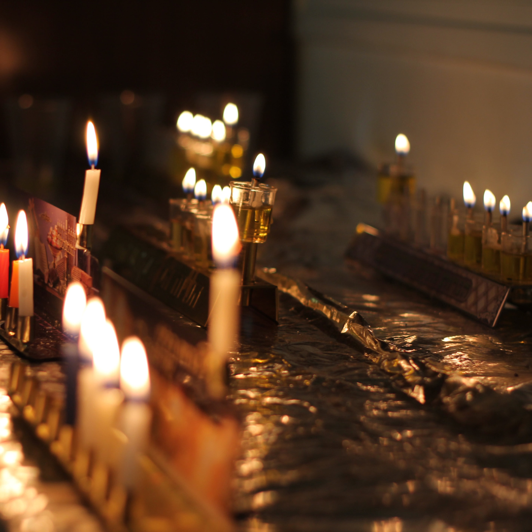Lit menorahs with candles and oil cups glowing on a reflective surface, celebrating Hanukkah.