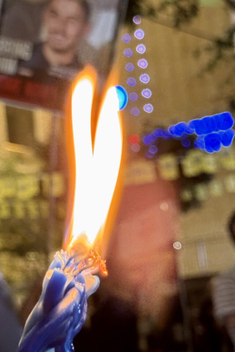 Close-up of a blue lighter with two flames, blurred city lights and a poster in the background.