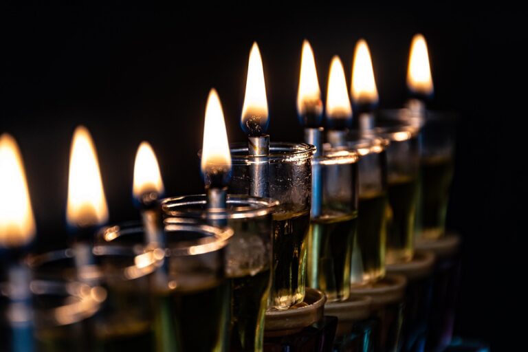 Close-up of a row of lit oil candles with glowing flames against a dark background.