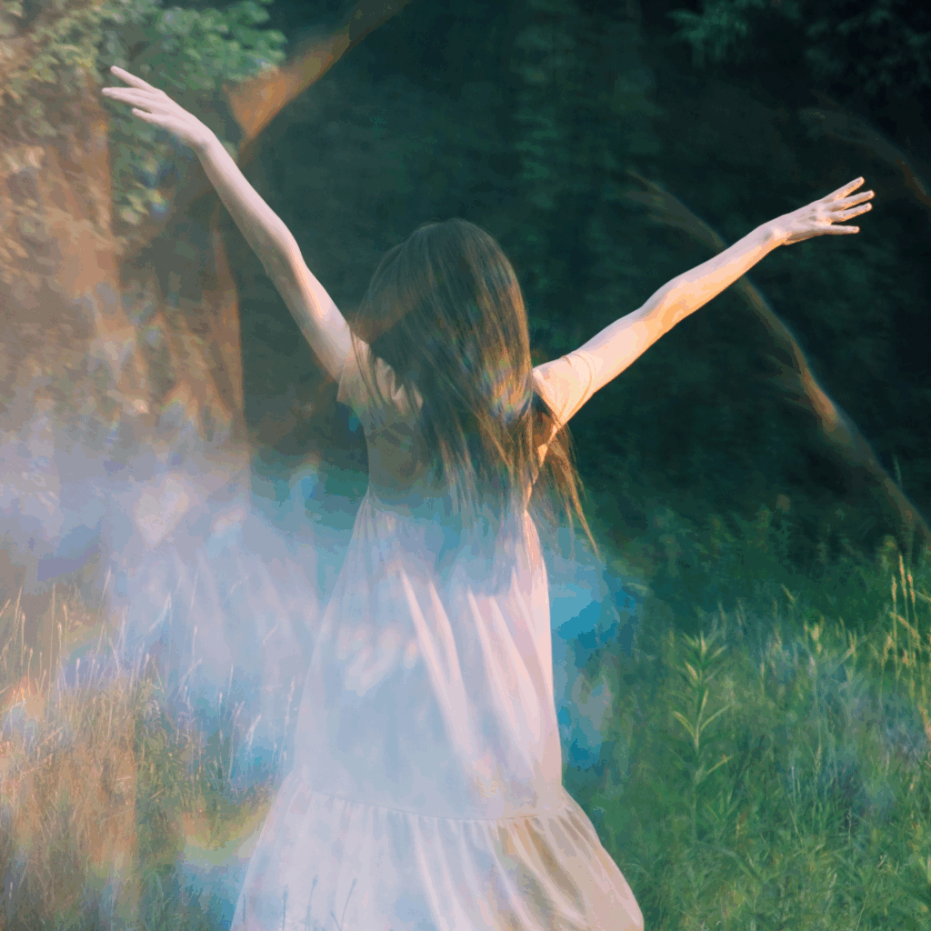 A person in a light dress stands in a sunlit meadow with arms raised, surrounded by soft, dreamy light.
