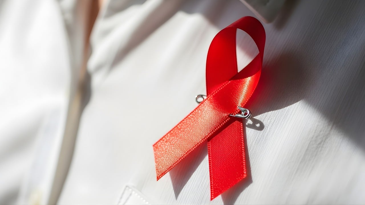 A red ribbon pinned to a white shirt, symbolizing awareness and support for HIV/AIDS.