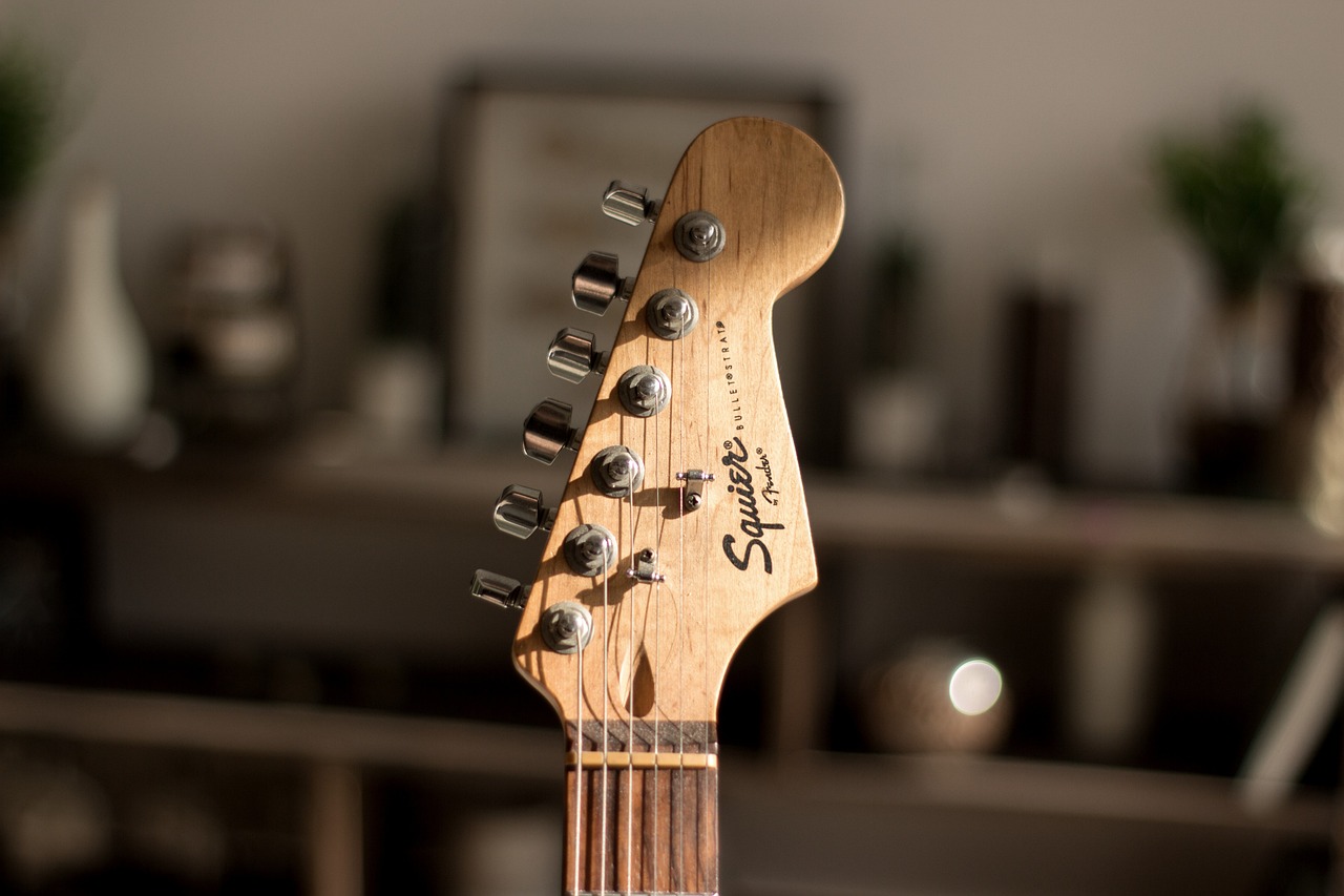 Close-up of a Squier electric guitar headstock with tuning pegs, blurred background.