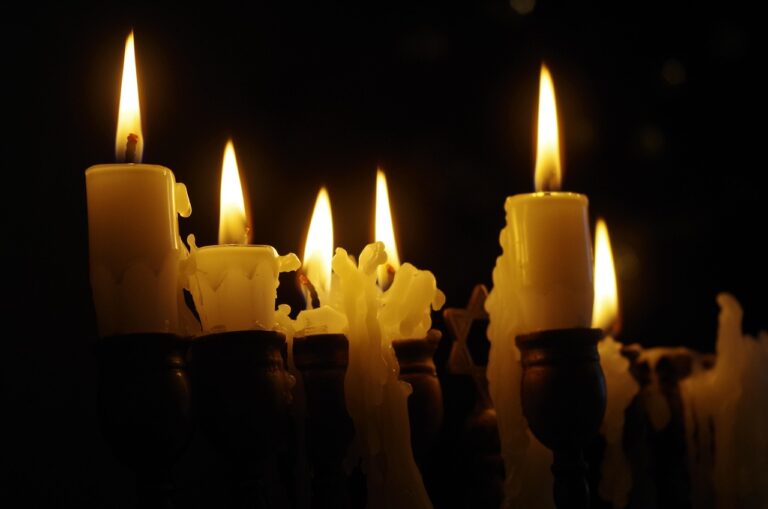 Close-up of seven lit candles with melting wax in a dark setting.