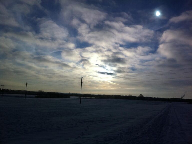 Snowy field under a cloudy sky with the sun and power lines visible in the background.