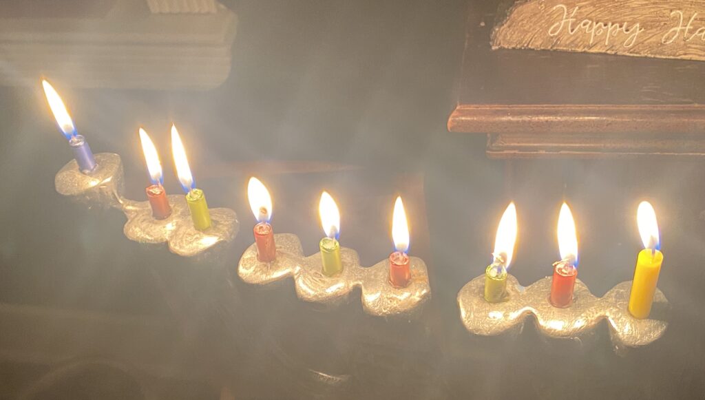 A menorah with nine brightly burning candles in various colors, lit for Hanukkah.