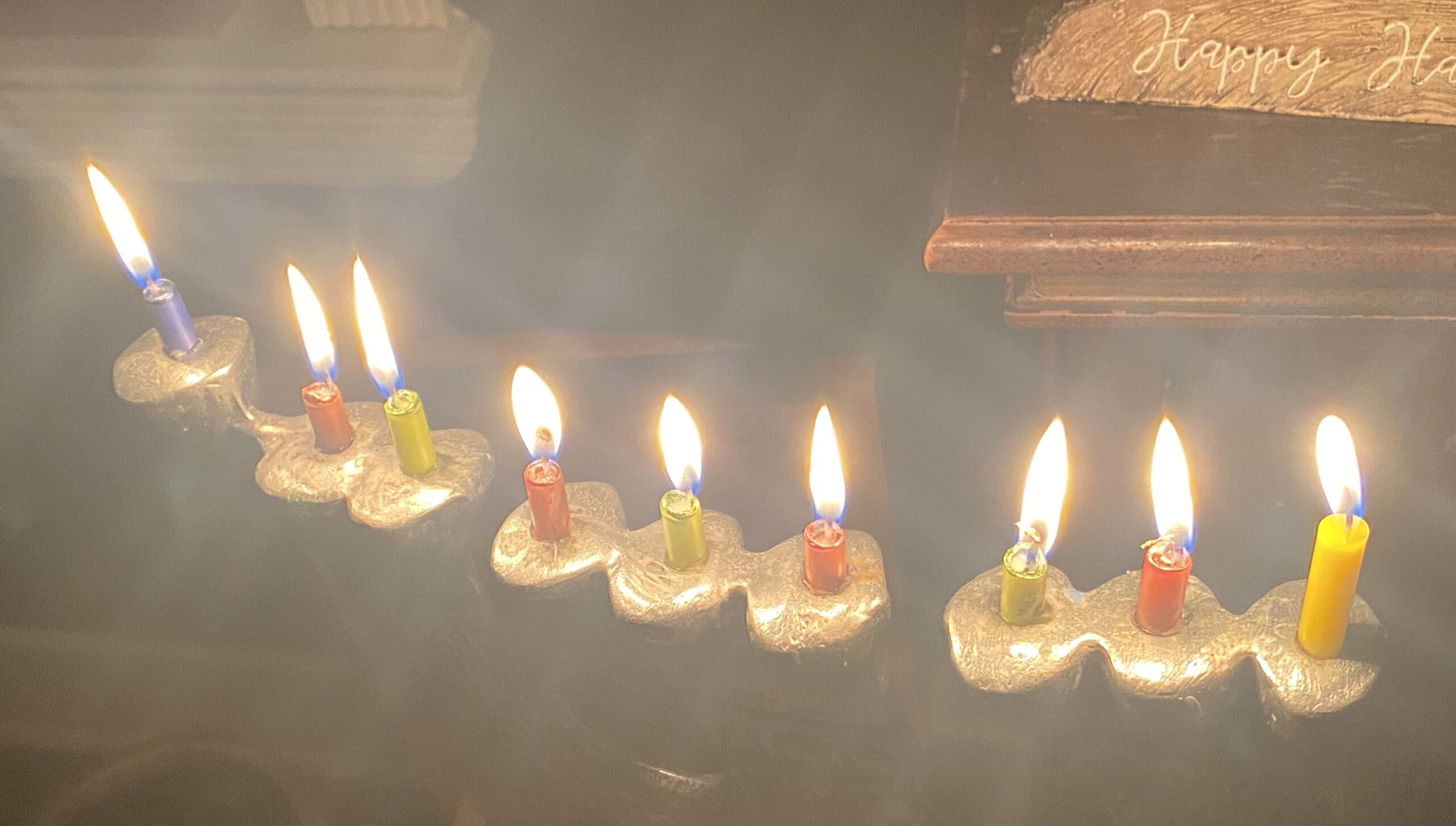 A menorah with nine brightly burning candles in various colors, lit for Hanukkah.