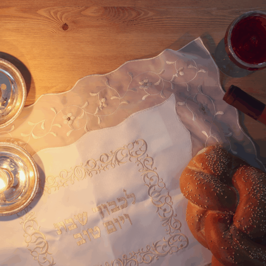 Challah bread, wine, and candles on a table with an embroidered cloth for a Shabbat meal.