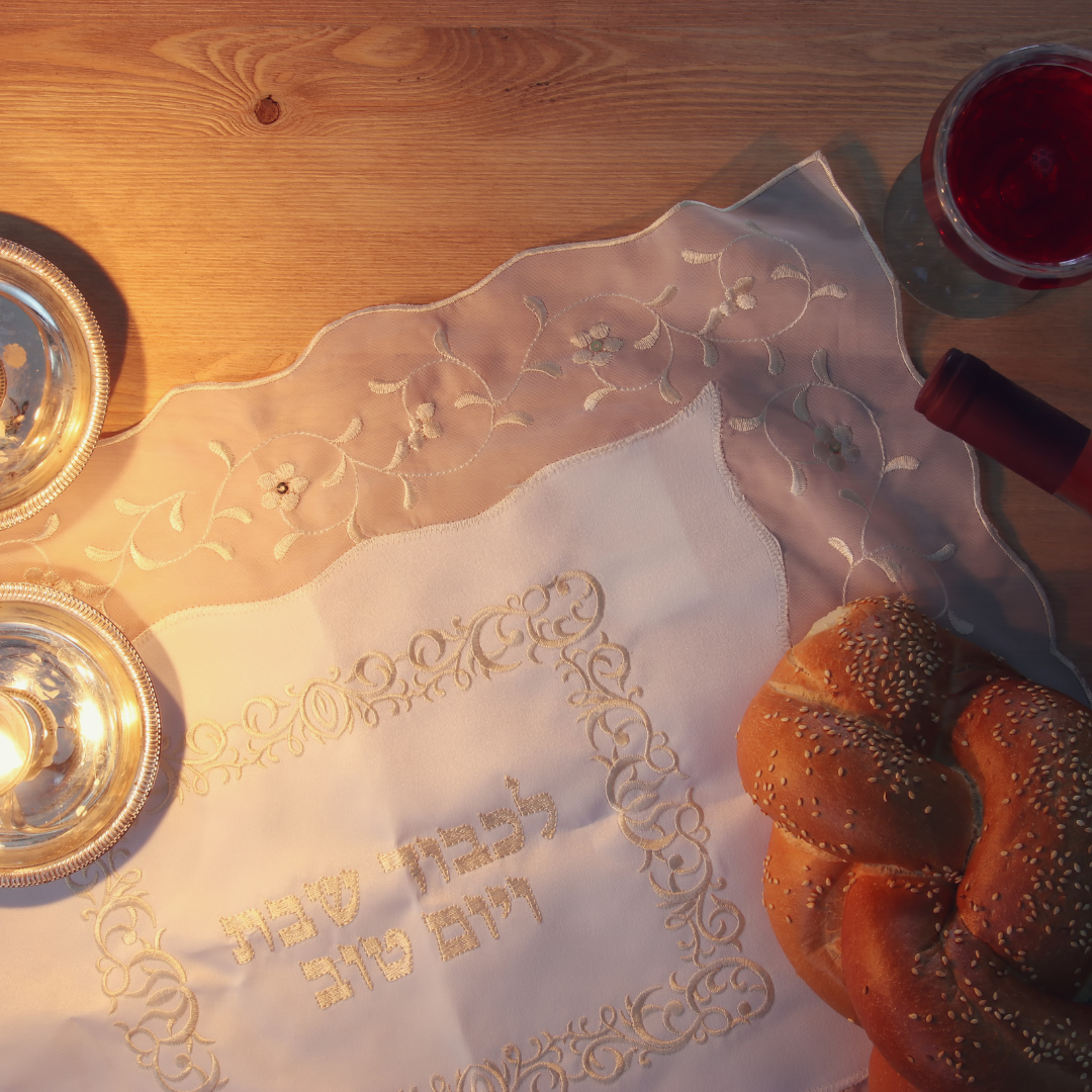 Challah bread, wine, and candles on a table with an embroidered cloth for a Shabbat meal.