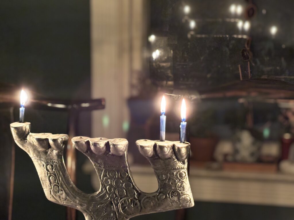 A menorah with two lit candles stands on a table, with a blurred background and mirror reflection.