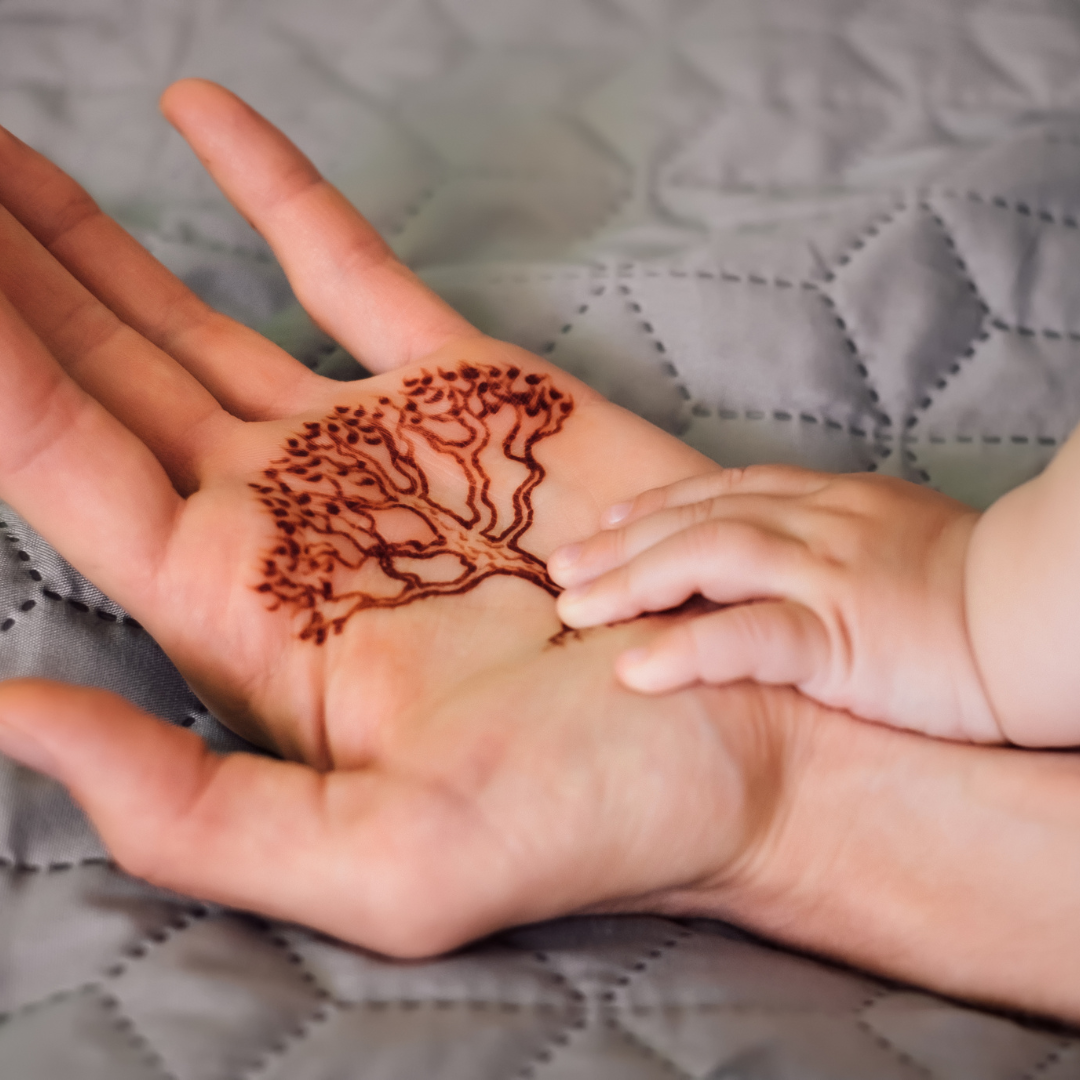A baby’s hand resting on an adult’s palm with a tree design drawn in henna.