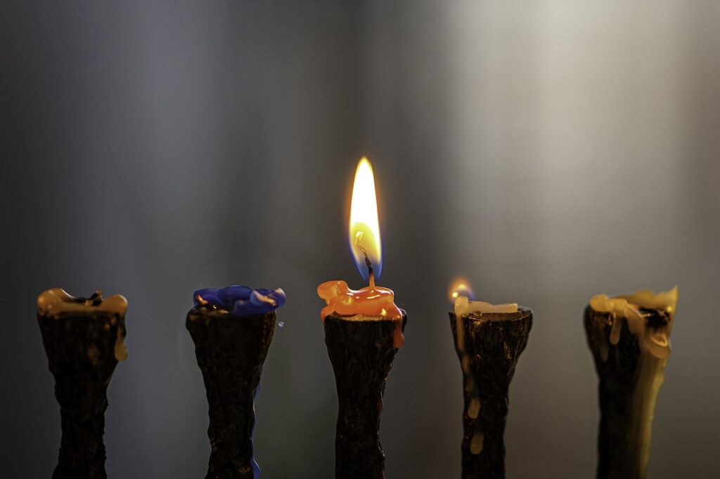 Five candle holders: one holds a lit candle, the others have melted wax and are unlit, background blurred.
