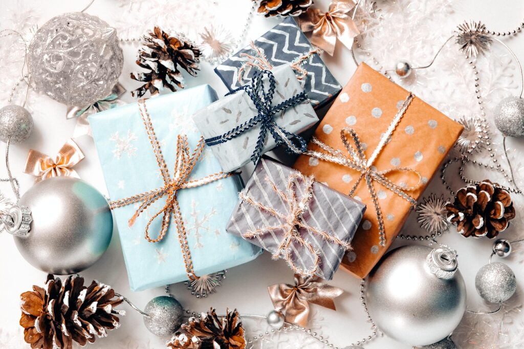 Gift boxes wrapped in festive paper surrounded by ornaments, pinecones, and silver holiday decorations.