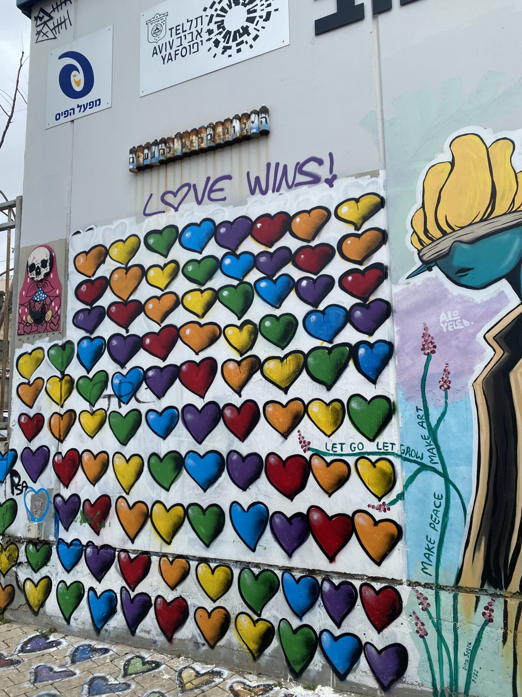 Colorful heart mural with LOVE WINS! written above, on a city wall with various graffiti and street art.