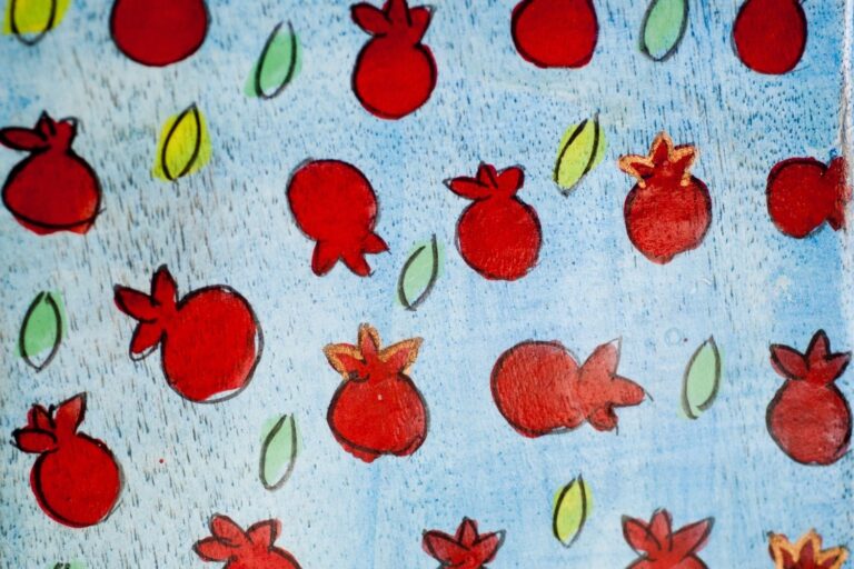 Red pomegranates and green leaves are scattered across a blue background in a playful, hand-drawn style.