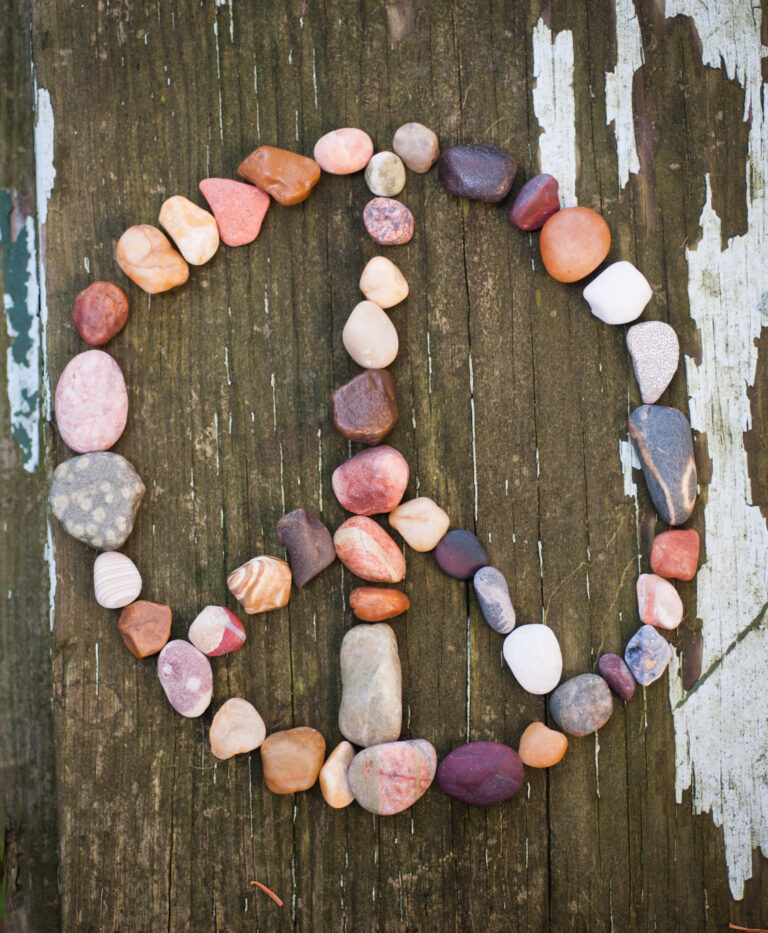 Peace sign made of colorful stones arranged on weathered wooden surface with peeling white paint.