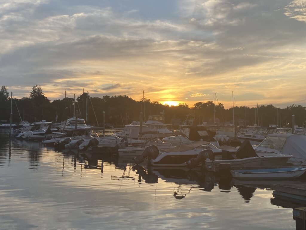 Boats docked at a marina with a colorful sunset and reflections on the water.