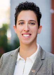 rabbi isabel de koninck is a Smiling person with short curly hair in a light blazer and white shirt, pictured outdoors.