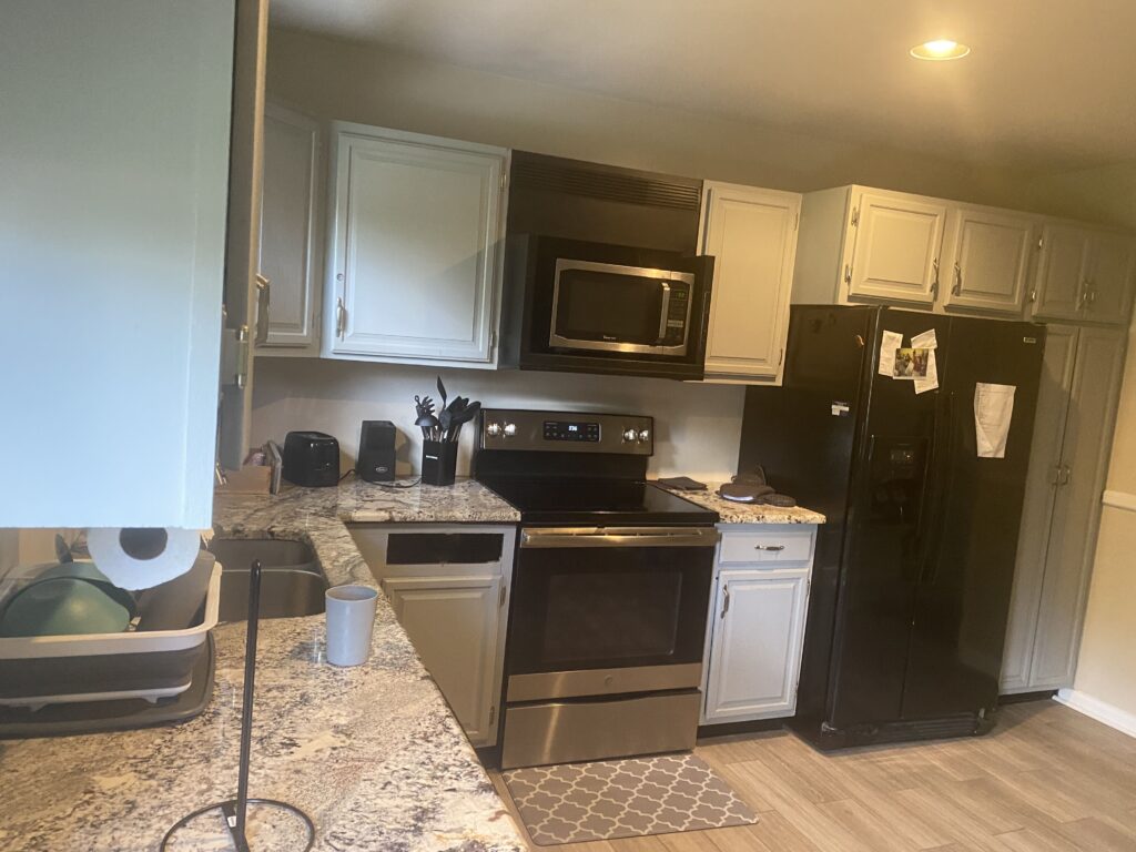 Modern kitchen with stainless steel appliances, black fridge, marble counters, and light gray cabinets.