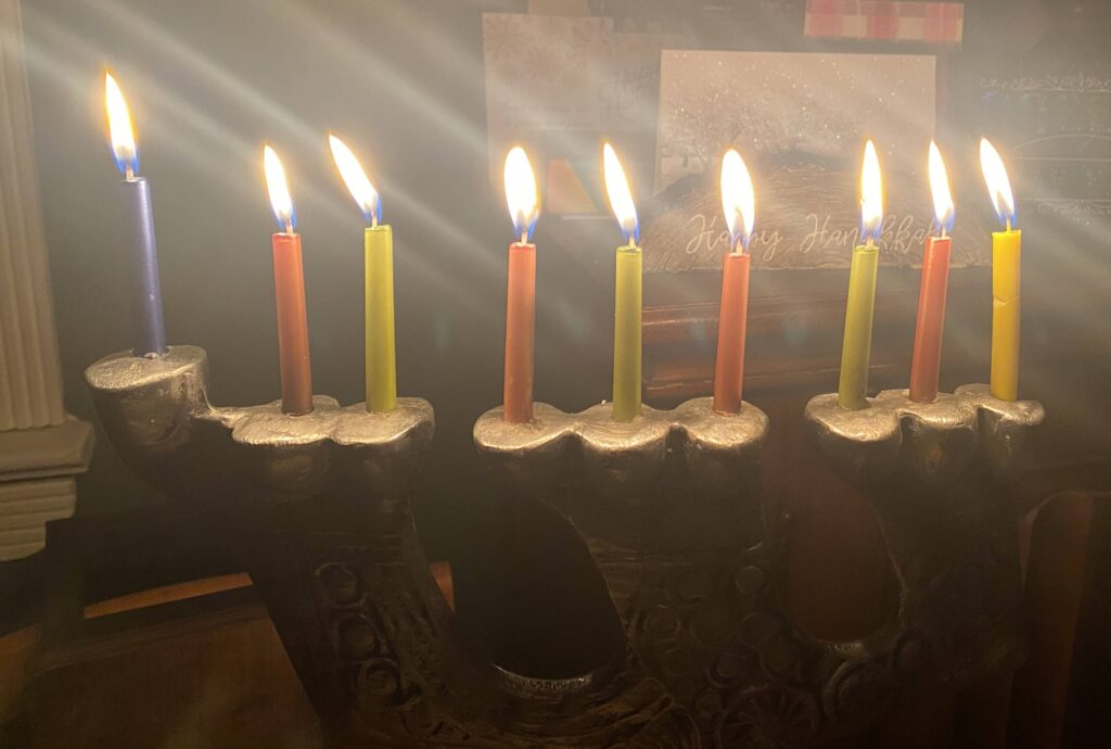 A lit menorah with nine candles, glowing brightly for Hanukkah on a dark background.