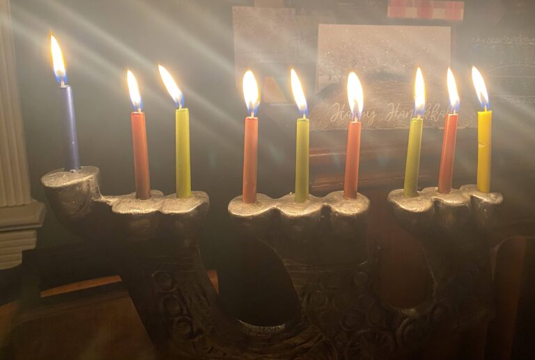 A lit menorah with nine candles, glowing brightly for Hanukkah on a dark background.