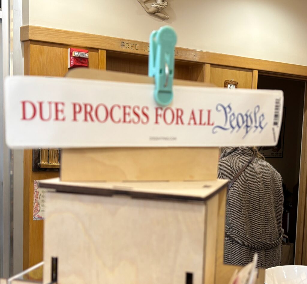 A sign clipped to a stand reads “DUE PROCESS FOR ALL People” in red and blue letters.