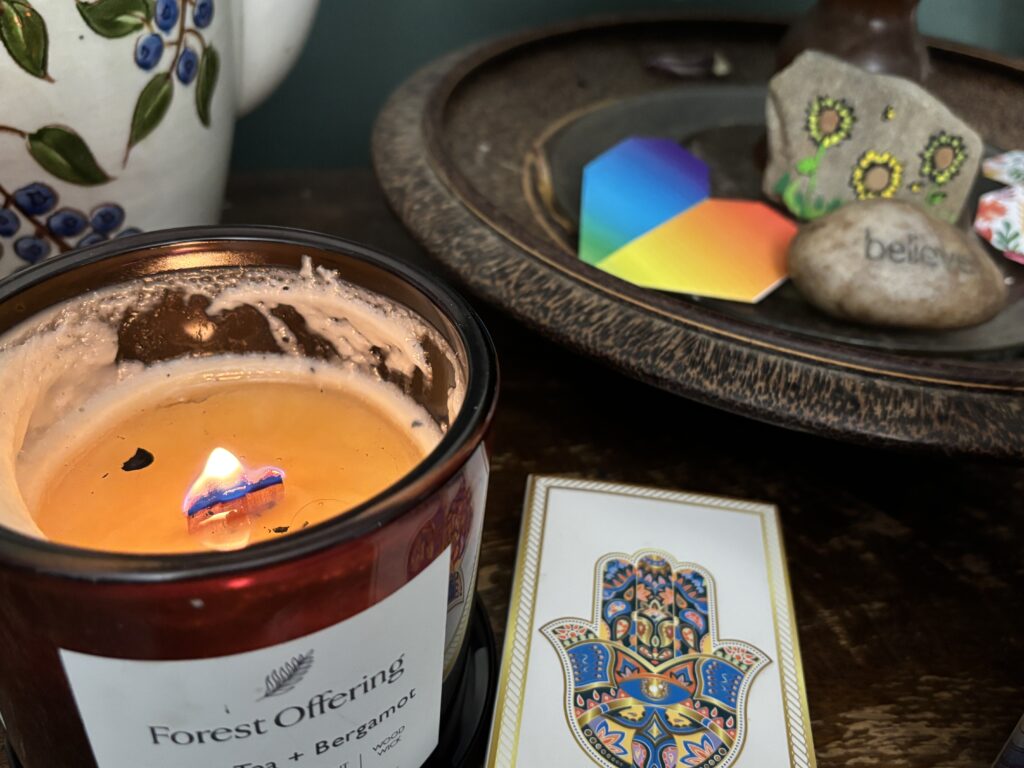A lit candle, a hamsa card, and stones on a tray, including one with the word believe engraved.