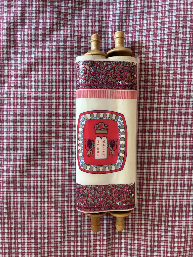 A decorated Torah scroll with red designs lies on a red and white checkered cloth.