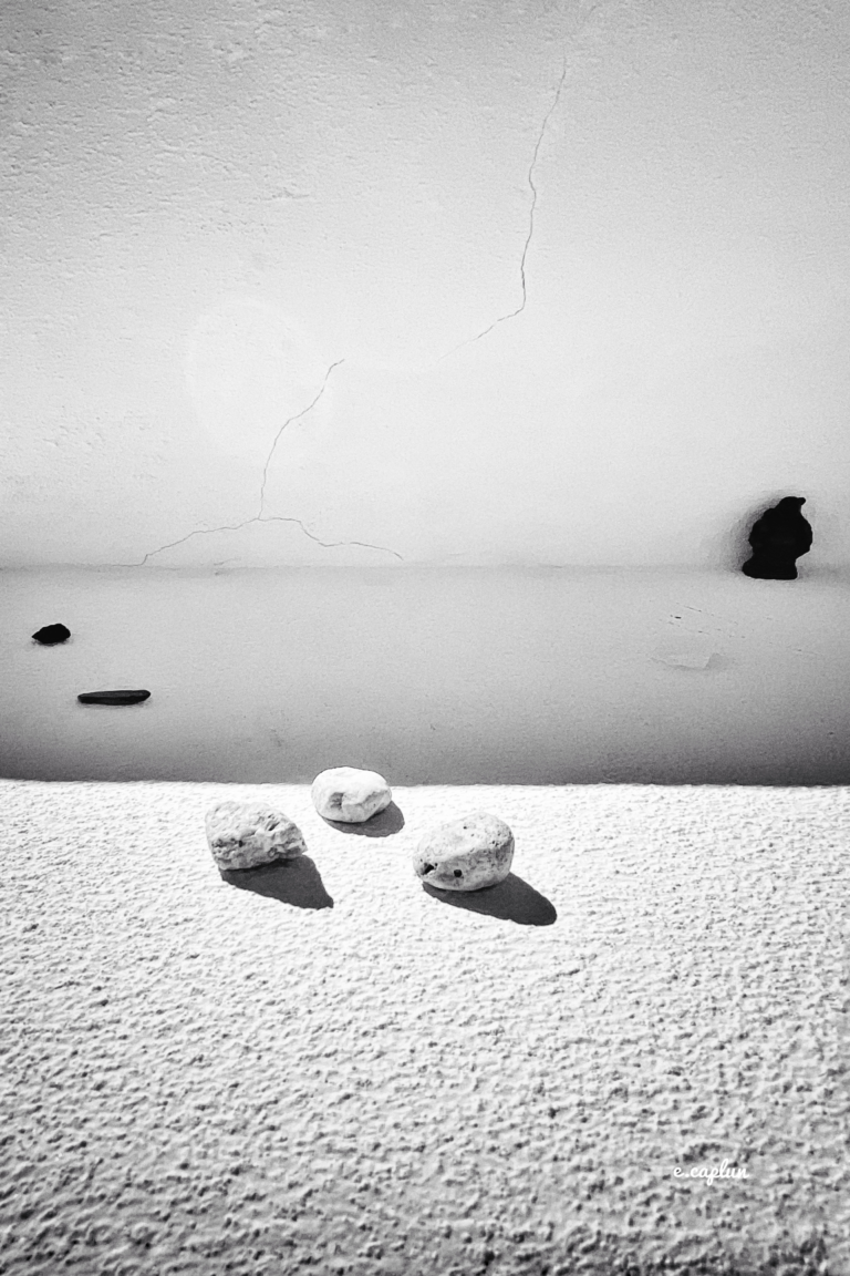 Three small stones on a textured ledge with a cracked, shadowed wall and two holes in the background.