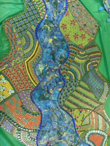 Colorful mosaic with a winding blue river, geometric patterns, flowers, and green, yellow, orange, and red tiles.