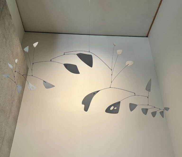 A hanging kinetic mobile featuring thin wire branches and abstract metal shapes suspended from the ceiling.