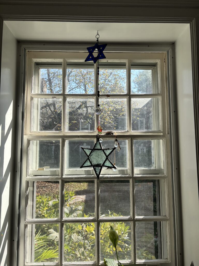 Two stained-glass Star of David ornaments hanging in a window.