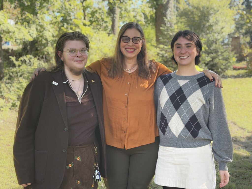 Three people smiling together outdoors with arms around each other.