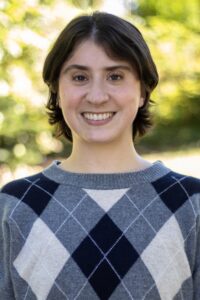 Vanessa Autitt - A smiling person with dark hair wearing a gray and navy blue argyle sweater.