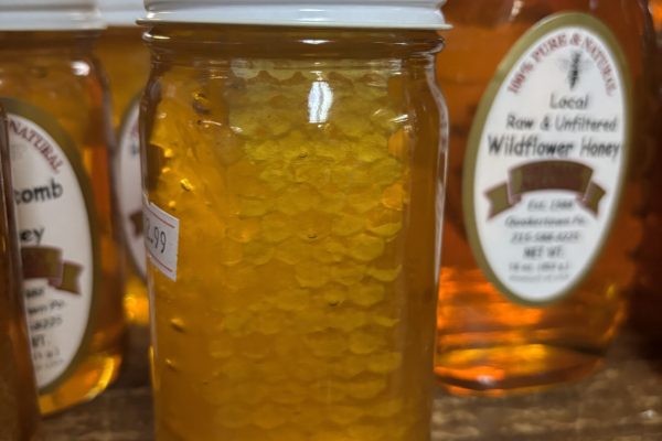 A jar of honey with honeycomb inside, displayed on a wooden shelf among other honey jars.