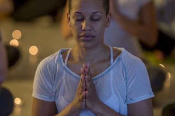 A person meditating with eyes closed, hands in prayer position, surrounded by soft lighting and candles.