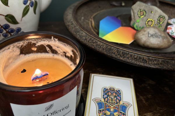 A lit candle, a hamsa card, and stones on a tray, including one with the word believe engraved.