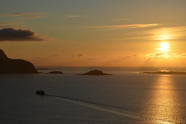 Sunset over calm sea with islands and a boat in the distance, casting a golden reflection on the water.