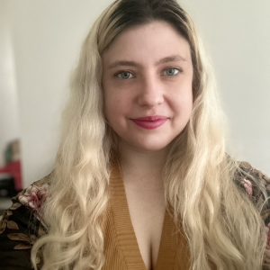 a woman is pictured with long blond hair with dark roots and a slight smile