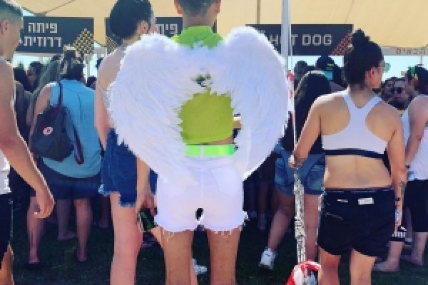 Person wearing angel wings and white shorts at an outdoor event with a crowd in the background.