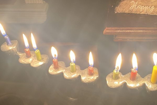 A menorah with nine brightly burning candles in various colors, lit for Hanukkah.