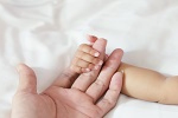 A babys hand gently holding an adults finger on a soft white background.