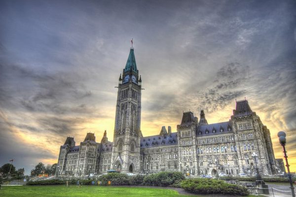 Historic building with a tall clock tower under a dramatic sky at sunset, surrounded by a grassy area.
