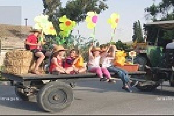 Children sitting on a hay-filled trailer decorated with colorful paper flowers, pulled by a tractor.