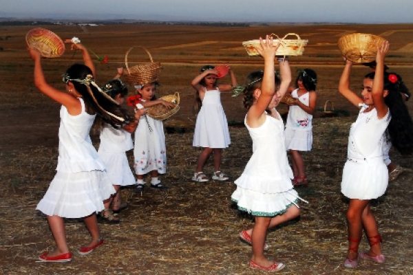 Group of girls in white dresses dancing with baskets in a field.